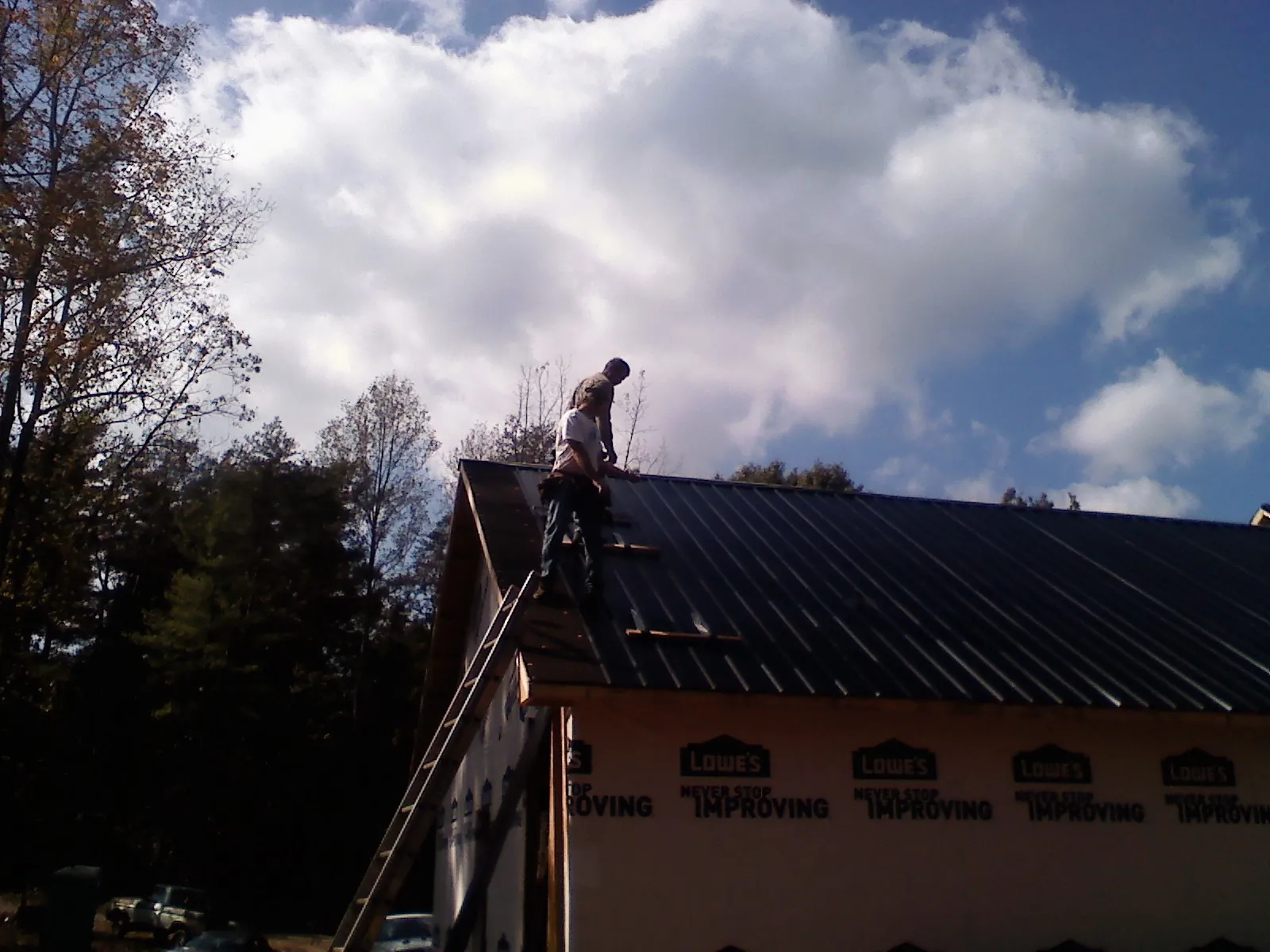 Roofer fastening dark metal panels high against a cloudy sky, from a Roof Inspection job in Sebastopol