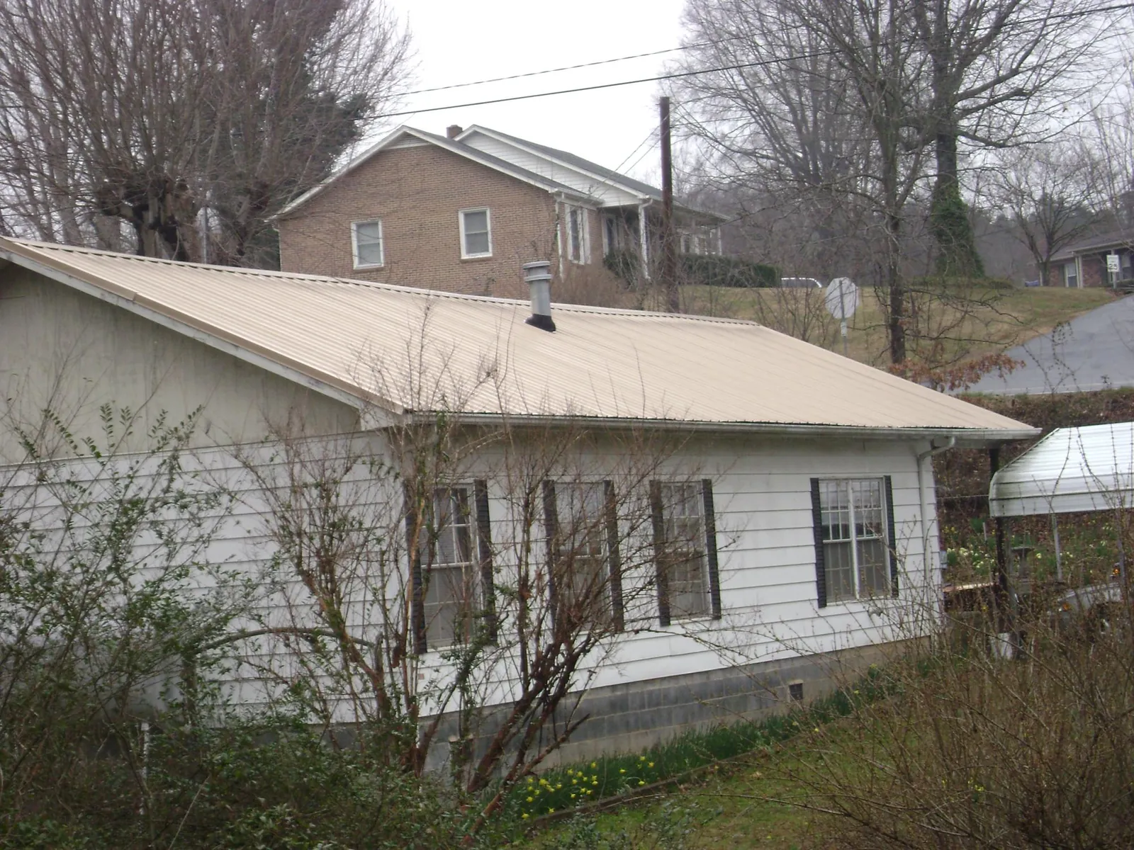 Tan metal roof on a white sided house set into a hillside — Commercial Roofing by Roofing Brothers in Sebastopol